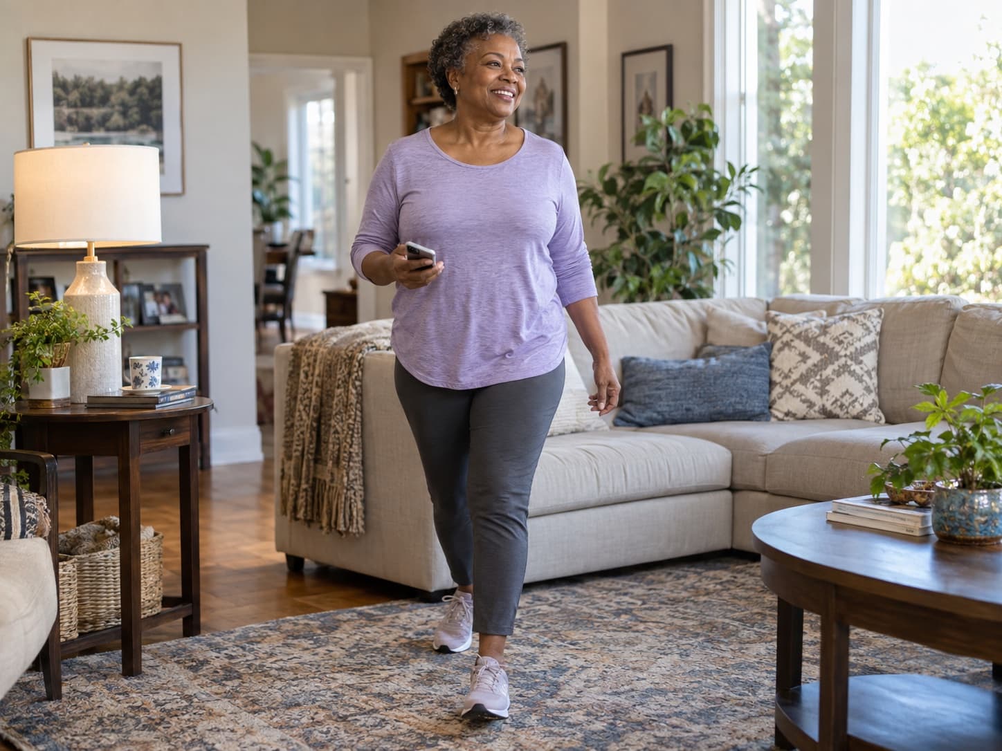 A smiling woman walking through her sunlit living room.